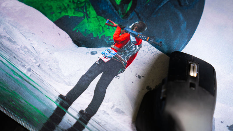 Close-up detail of the survivor character on the Oilrats Frozen Paradise deskmat, standing on frozen terrain beneath a towering green skull monument in a snowy Rust-inspired landscape.