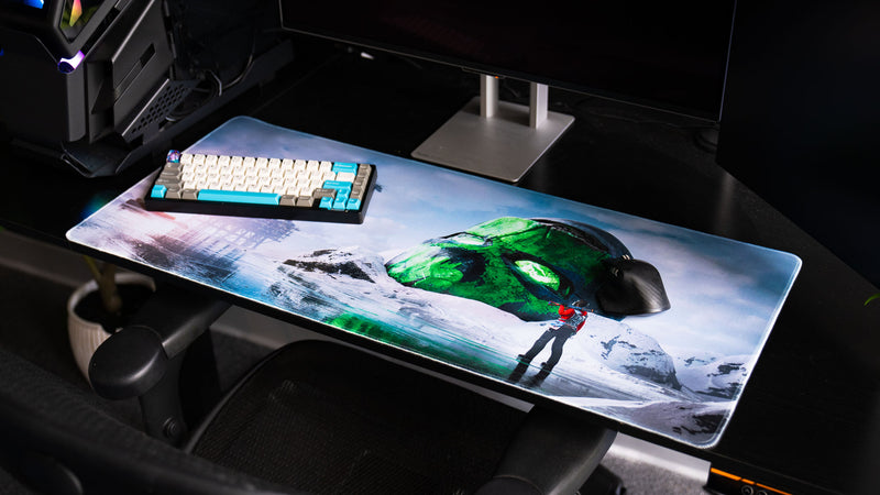 Oilrats Frozen Paradise deskmat displayed on a gaming desk, featuring a giant glowing green skull in a snowy landscape, reflective frozen water, distant offshore rig, and a lone survivor exploring the frozen wasteland.