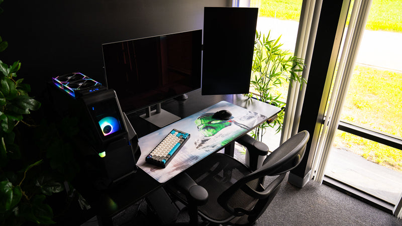 Oilrats Frozen Paradise deskmat displayed in a bright gaming setup featuring dual monitors, a custom PC, mechanical keyboard, and the frozen skull artwork extending across the desktop workspace.