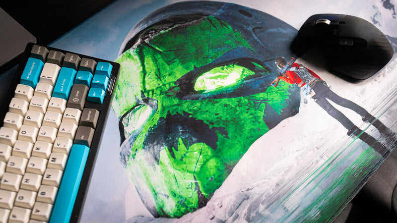 Detailed close-up of the Oilrats Frozen Paradise deskmat featuring a glowing green skull partially buried in snow beside a lone survivor, showcasing the artwork’s vibrant colors and high-definition print quality.
