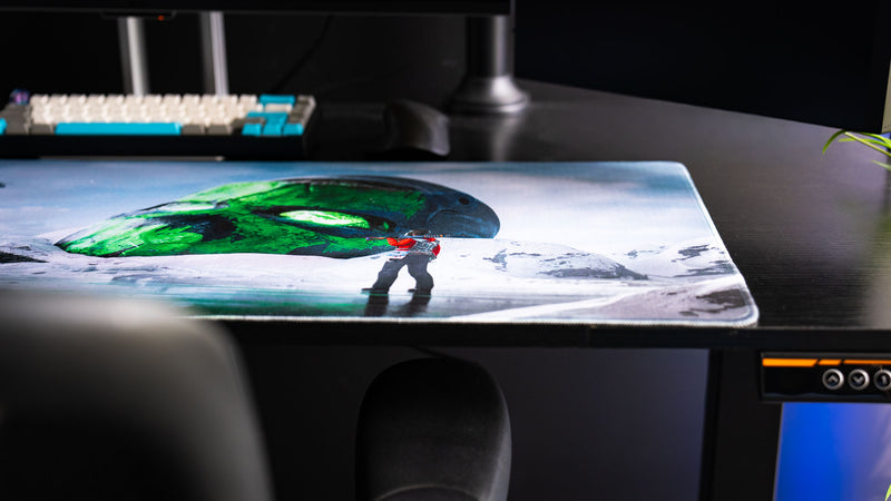 Close-up of the Oilrats Frozen Paradise deskmat featuring a lone survivor standing on reflective ice before a massive glowing green skull embedded in a snowy frozen landscape, showcasing the artwork’s detailed environmental design.
