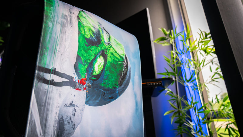 Side-angle view of the Oilrats Frozen Paradise deskmat highlighting the towering green skull emerging from a frozen landscape, with a lone survivor standing before it and bright green eyes glowing through the icy scene.