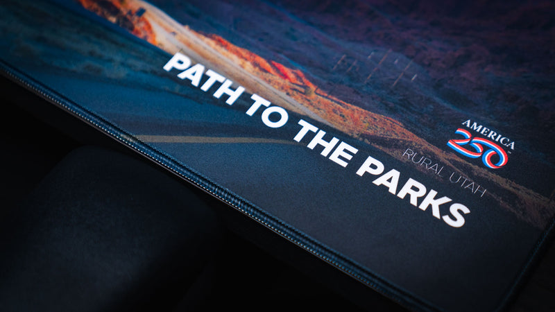 Close-up of the Path to the Parks America 250 deskmat showing the printed title, America 250 logo, Rural Utah label, road artwork, and stitched edge detail.