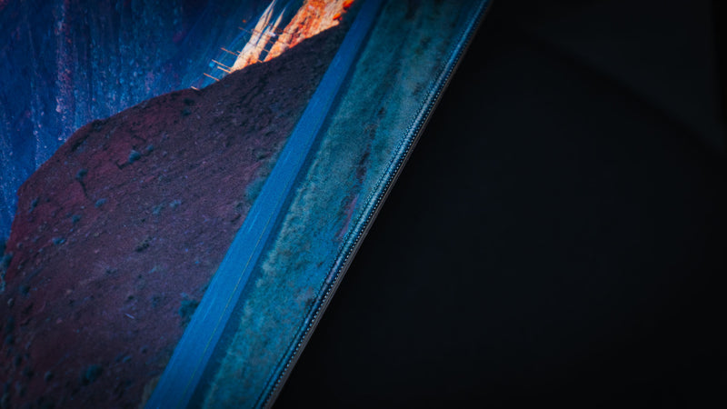 Close-up edge detail of the Path to the Parks America 250 deskmat showing the printed Utah road scene, dark desert tones, and stitched border.