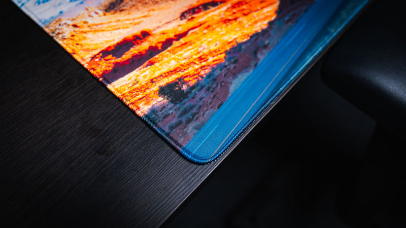Close-up corner detail of the Path to the Parks America 250 deskmat showing the printed Utah road artwork, vibrant red rock colors, and stitched edge finish.