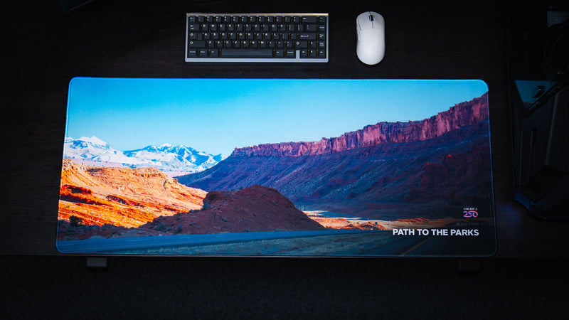Wide overhead shot of the Path to the Parks America 250 deskmat featuring a vivid rural Utah desert scene with red cliffs, snowy mountains, and road details.