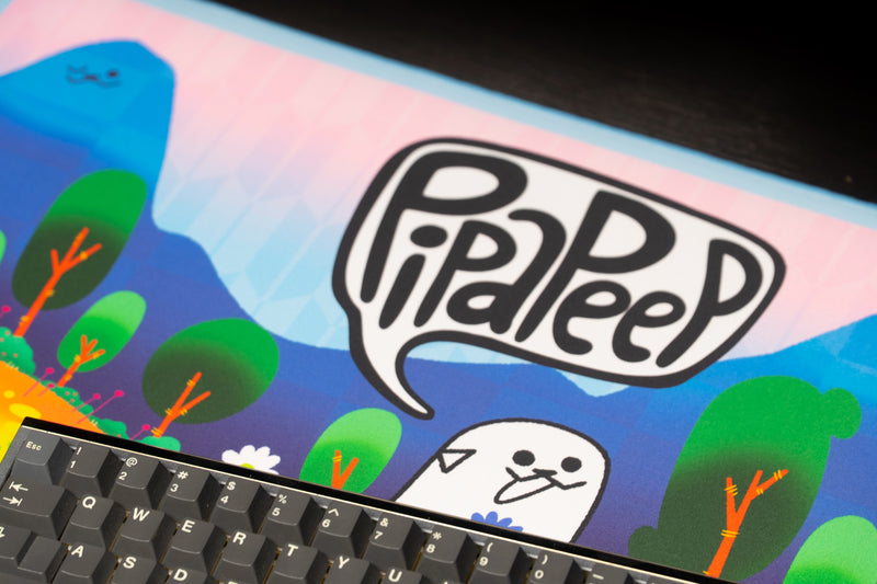 Close-up of the Pippa Peep logo and white character on the Pipaland deskmat beside a keyboard.