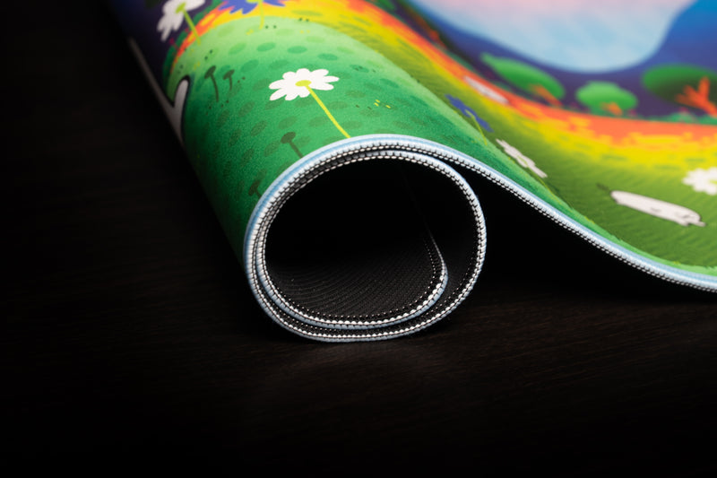 Close-up of the rolled Pipaland deskmat showing its light-blue stitched edge, printed flowers, and black backing.
