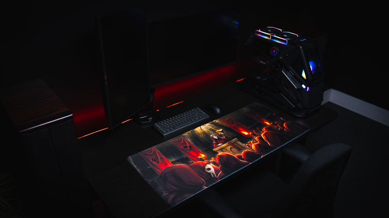 Pravus Crimson Convocation deskmat displayed in a premium gaming setup featuring a mechanical keyboard, dual monitors, and a PC with dramatic red ambient lighting.