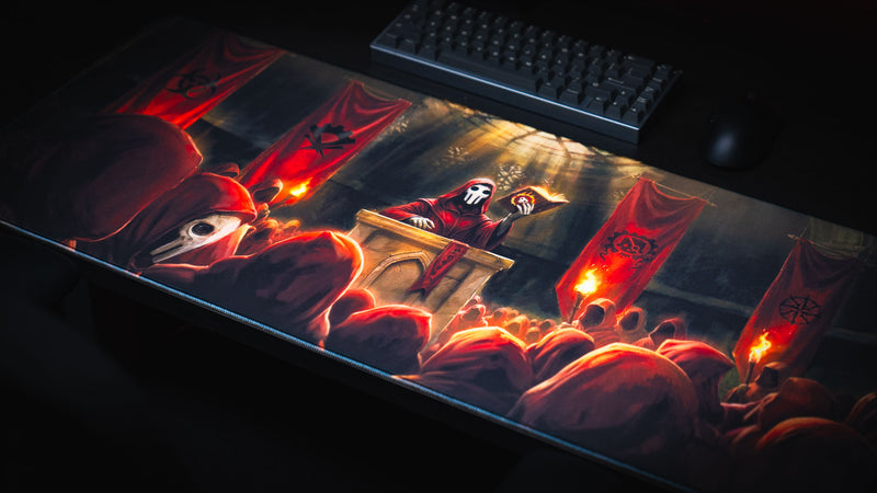 Angled view of the Pravus Crimson Convocation deskmat featuring a masked cult leader addressing crimson-robed followers with dramatic torchlit fantasy artwork on a gaming desk.