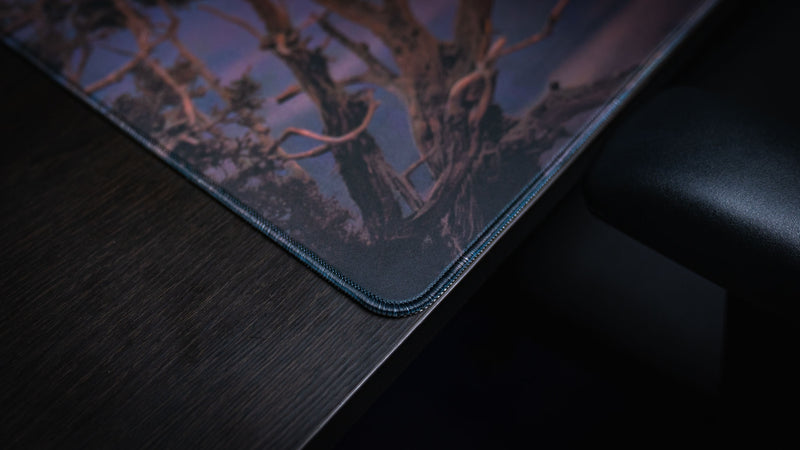 Close-up of the Raven America 250 deskmat corner showing dark canyon artwork, desert tree detail, fabric texture, and premium stitched edge.
