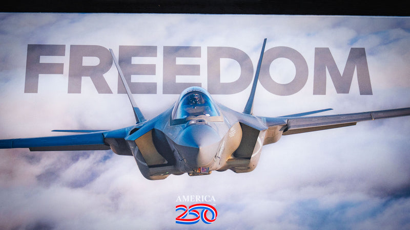 Close-up of the Freedom in the Sky America 250 deskmat featuring a fighter jet, cloudy sky artwork, and bold FREEDOM text.
