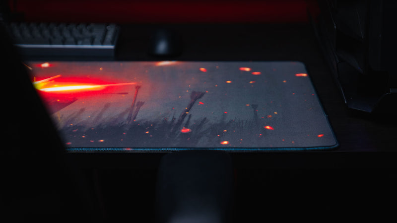Side-angle view of the Ricochet gaming deskmat highlighting the fiery impact effect, premium stitched edges, and immersive battlefield artwork on a desktop setup.