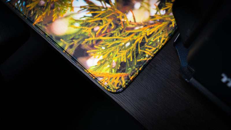 Close-up of the Robin wildlife deskmat corner showcasing premium stitched edges, vibrant juniper foliage, and the high-resolution fabric print finish.