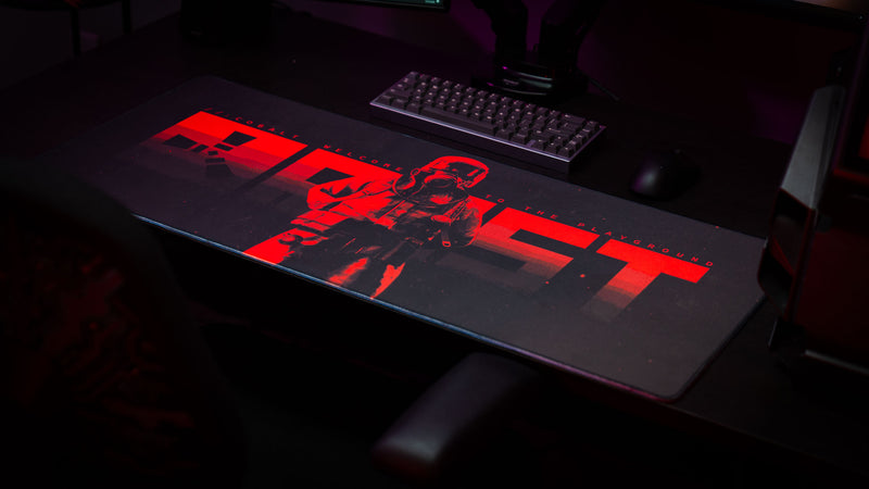 Wide-angle gaming setup featuring the Welcome to Rust deskmat with red hazmat artwork, mechanical keyboard, and dark RGB lighting.
