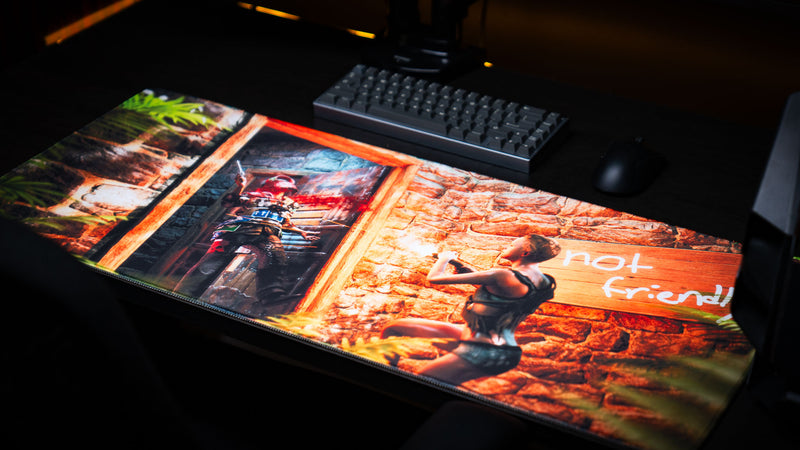 The Doorcamper / Angle 3 Rust deskmat displayed in a gaming setup with a mechanical keyboard and mouse, showcasing a close-range stone base firefight, a "Not Friendly!!" warning sign, and detailed tropical jungle surroundings
