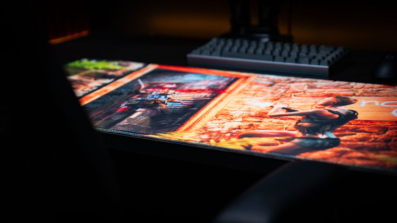 The Doorcamper / Angle 3 Rust deskmat displayed on a gaming desk, highlighting an intense doorway ambush scene with a stone base, dramatic firefight, tropical foliage, and premium stitched-edge construction.