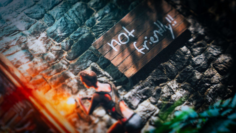 Close-up of The Doorcamper / Angle 1 Rust deskmat highlighting the iconic "Not Friendly!!" warning sign on a stone base wall, with detailed survivor artwork and vibrant jungle surroundings.