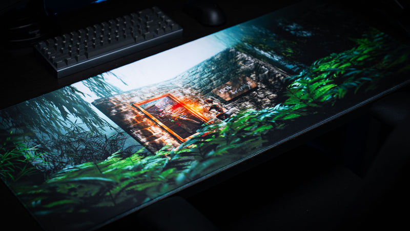 The Doorcamper / Angle 1 Rust deskmat featuring a hidden jungle stone base under attack, with dense tropical foliage, dramatic lighting, and a premium stitched-edge gaming surface displayed on a desk.