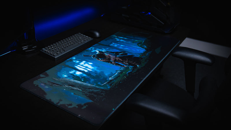 Official Rust Hunted XXL deskmat on a desktop gaming setup, featuring a lone survivor in a moonlit forest with a premium stitched-edge cloth surface.