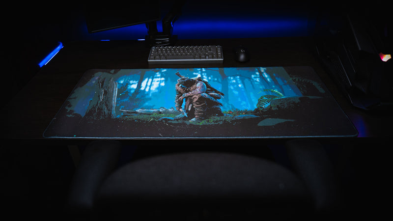 Official Rust Hunted XXL deskmat displayed across a desktop gaming setup, featuring a lone survivor in a moonlit forest on a premium stitched-edge cloth surface.