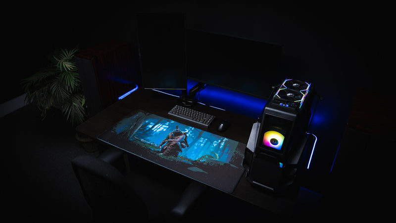 Official Rust Hunted XXL deskmat displayed in a complete PC gaming setup, featuring a lone survivor in a moonlit forest with a premium stitched-edge cloth surface.
