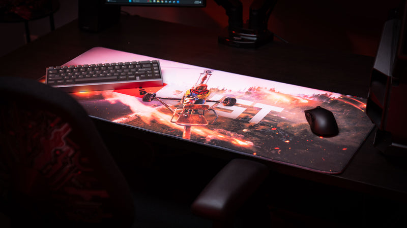 Gaming desk setup featuring the Rust “Minicopter Joyride” deskmat with fiery aerial artwork, mechanical keyboard, and gaming mouse.