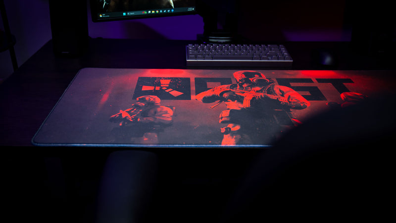 Rust Scientist Trio deskmat displayed on a gaming desk with dramatic red ambient lighting, showcasing the iconic scientist artwork and premium stitched-edge design.