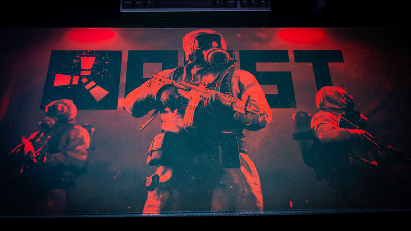 Full artwork view of the Rust Scientist Trio deskmat featuring three armed scientists beneath the Rust logo, illuminated by dramatic red lighting and atmospheric effects.