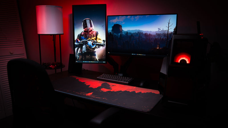 Dark gaming battlestation featuring the Satellite Dish XXL deskmat with red atmospheric Rust-inspired artwork, dual monitors, and ambient red lighting.