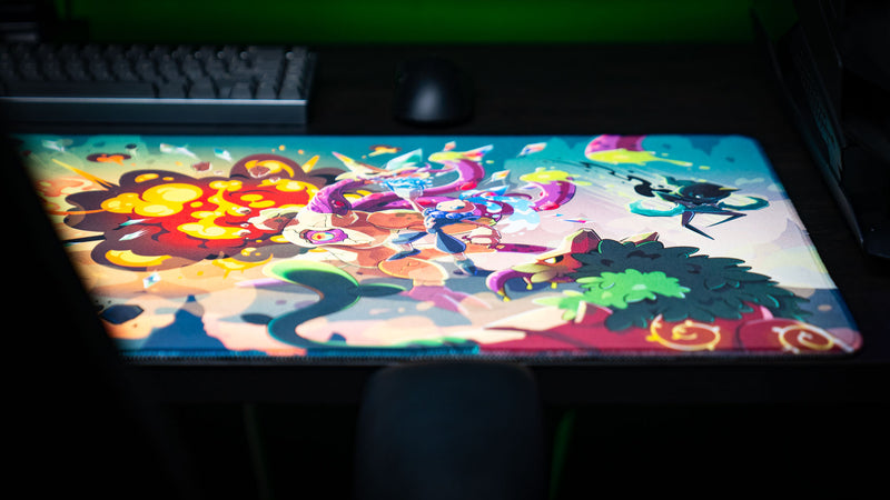 Close-up of the Sedi-mat deskmat by Pokedex Studios featuring colorful fantasy creatures in an explosive battle with vibrant artwork, stitched edges, and a premium gaming desk setup.