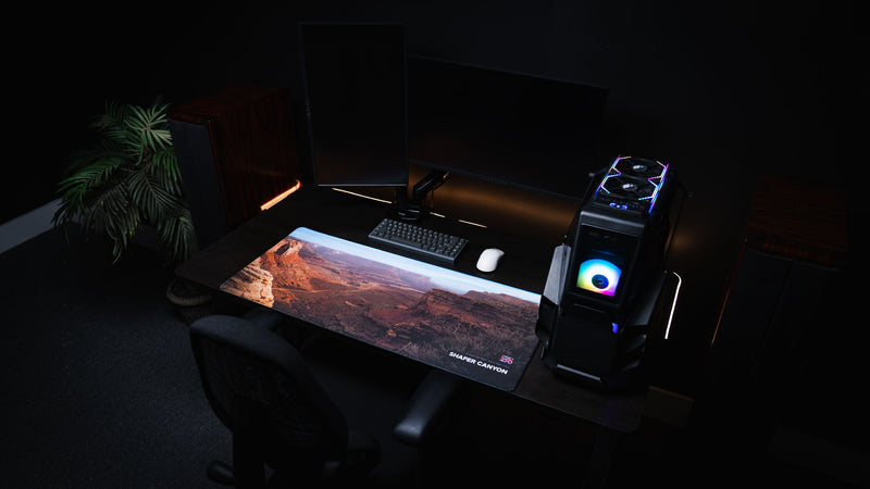 Shafer Canyon America 250 deskmat displayed in a dark RGB desk setup with Canyonlands desert scenery, keyboard, mouse, PC, and warm accent lighting.