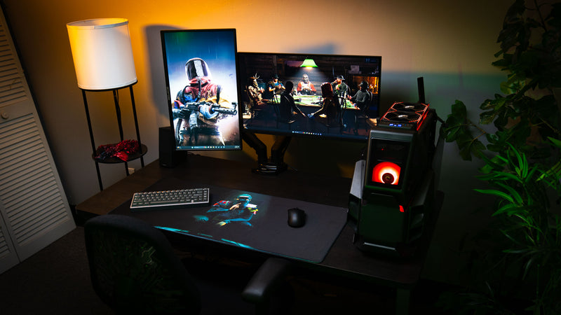 The Shh Rust deskmat showcased in a complete gaming battlestation with dual monitors, RGB gaming PC, mechanical keyboard, and the iconic shushing character artwork.