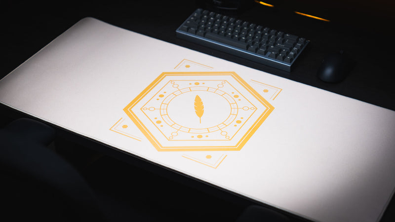 Angled view of the Feathered Host deskmat with gold emblem and black keyboard