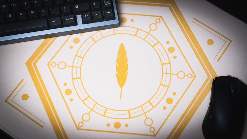 Close-up of the gold feather emblem on the Feathered Host deskmat beside a keyboard