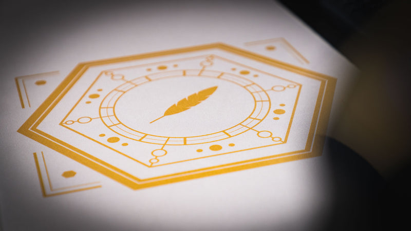 Detail of the gold feather inside the geometric sigil on the Feathered Host deskmat