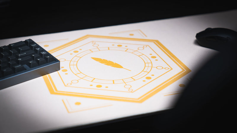 Angled close-up of the gold feather and geometric sigil on the Feathered Host deskmat