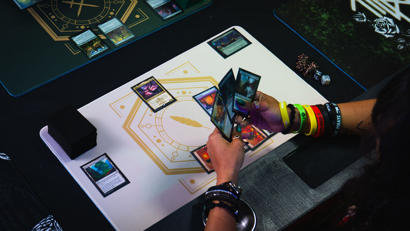 Close overhead view of trading cards and a player's hand on the Feathered Host playmat
