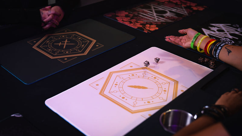 Dice rolling on the Feathered Host playmat beside a dark green playmat