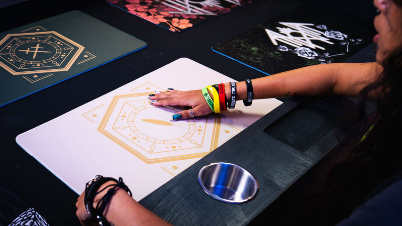 Player's hand resting on the Feathered Host playmat during a tabletop game