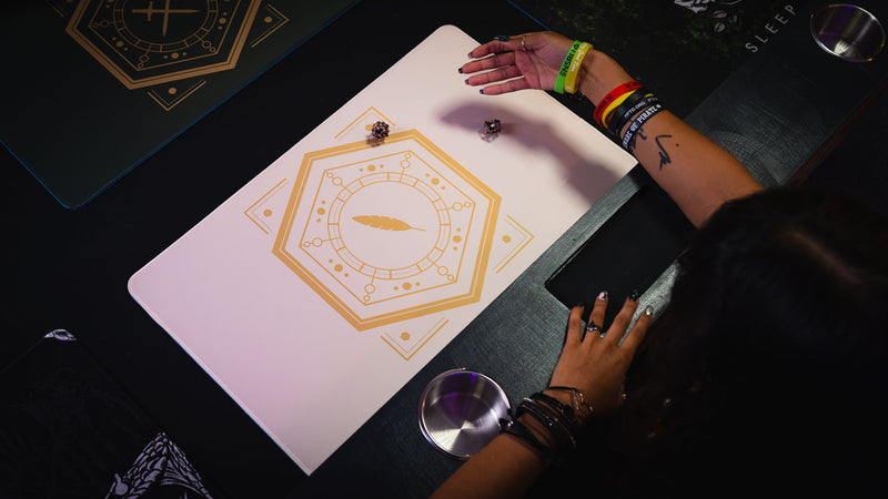 Overhead angle of two dice on the Feathered Host playmat's gold feather sigil