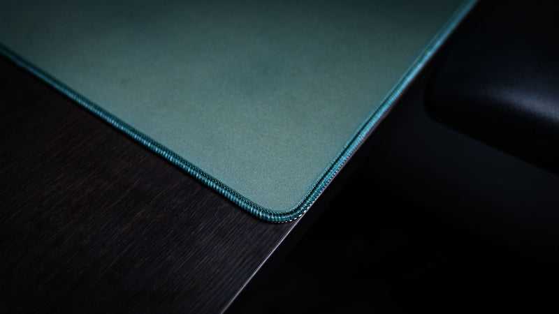 Close-up of the rounded corner and stitched edge of green House Veridian deskmat