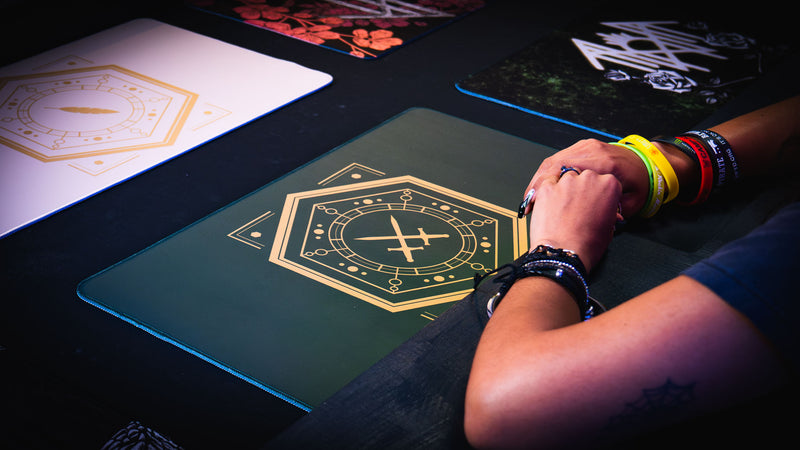 Angled close-up of the gold crossed-swords emblem on the deep green House Veridian playmat