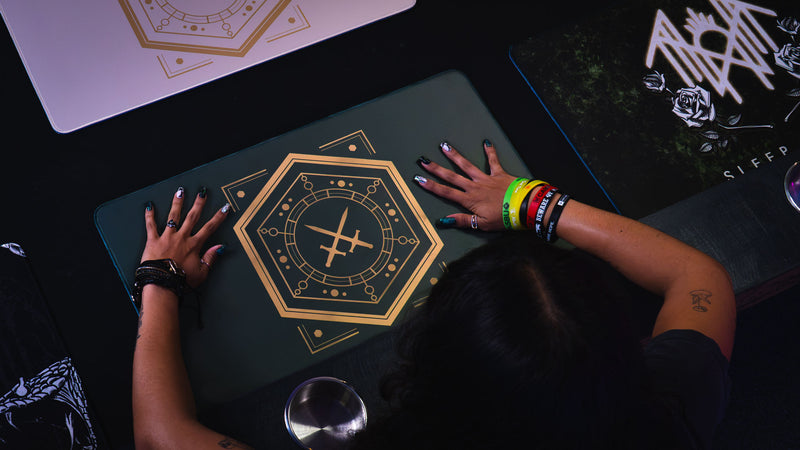 Player's hands on the House Veridian playmat beside other Sleep Token playmats at a gaming table