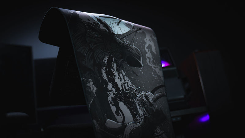 Close view of The Battle deskmat draped over a chair, showing the hooded figure and creature artwork