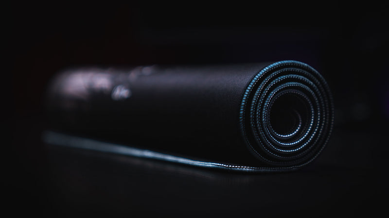 Rolled The Battle deskmat showing its dark fabric, stitched edge and rubber underside