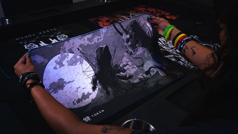 Player holding the flexible The Battle Sleep Token playmat by its corners to display the full artwork