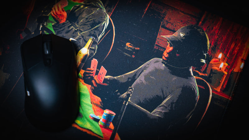 Close-up of the Sleight of Hand Rust gaming deskmat featuring a survivor holding poker cards beside a gaming mouse in a dimly lit cabin poker game.