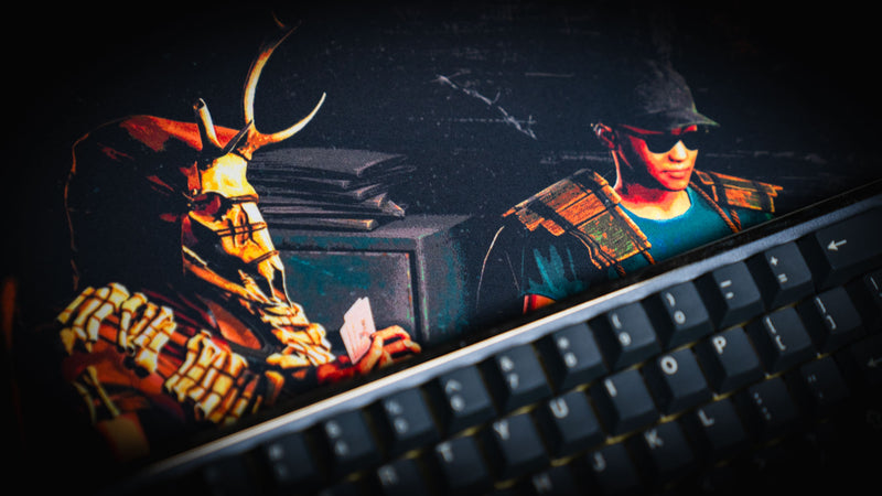 Close-up of the Sleight of Hand Rust gaming deskmat featuring poker players, a deer skull mask survivor, and detailed cabin artwork beside a mechanical keyboard.