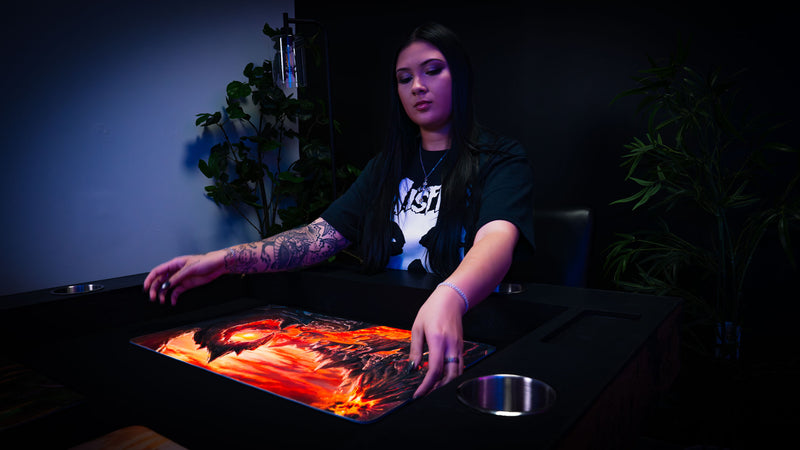 Smoldering Mountain playmat displayed on a tabletop, featuring a fiery volcanic landscape with glowing lava flows and towering obsidian peaks.